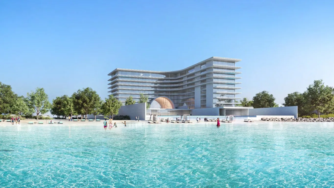 Curved terraced building behind a turquoise lagoon and sandy beach lined with trees